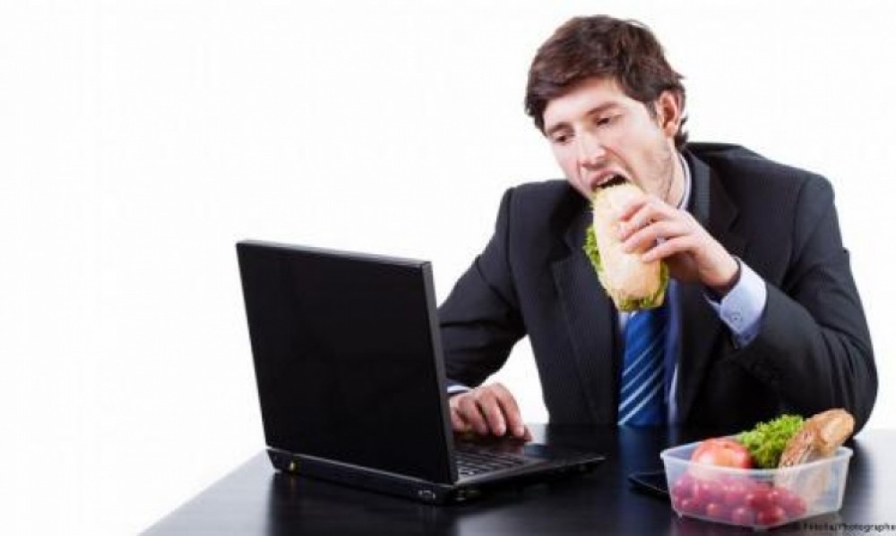 رجل يأكل وهو يعمل خلف مكتبه