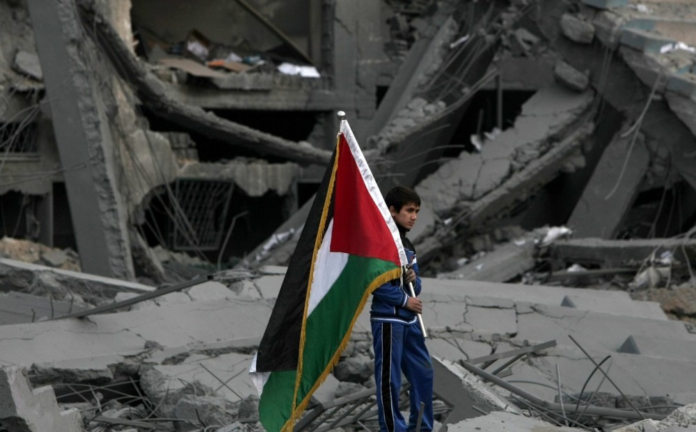 طفل يحمل علم فلسطين فوق أنقاض منزله الذى دمر نتيجة العدوان الإسرائيلي على قطاع غزة