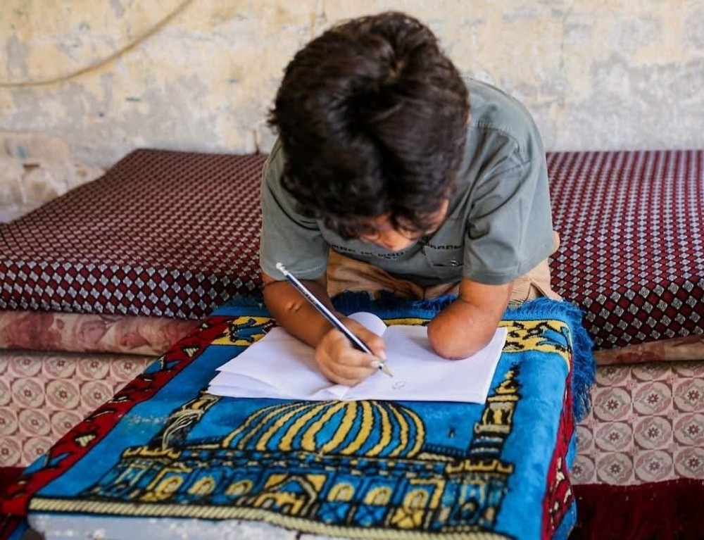 كنان أبو جبة.. طفل من غزة يخطّ بيده الوحيدة أمل العودة إلى مقاعد الدراسة