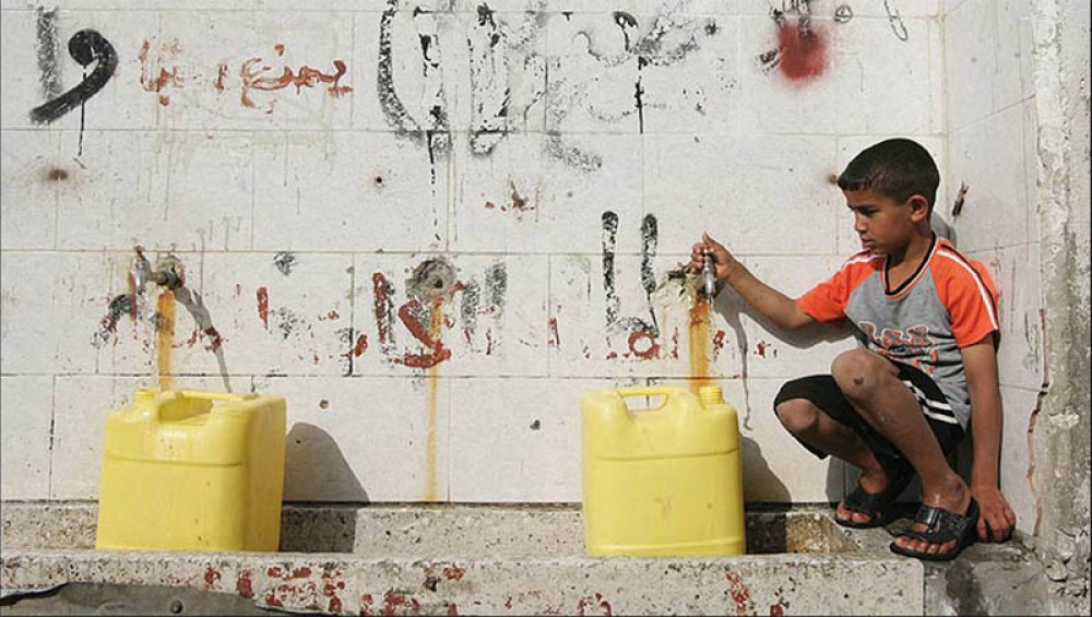 طفل غزي ينتظر امتلاء الجالونات بالمياه في محطة تحلية