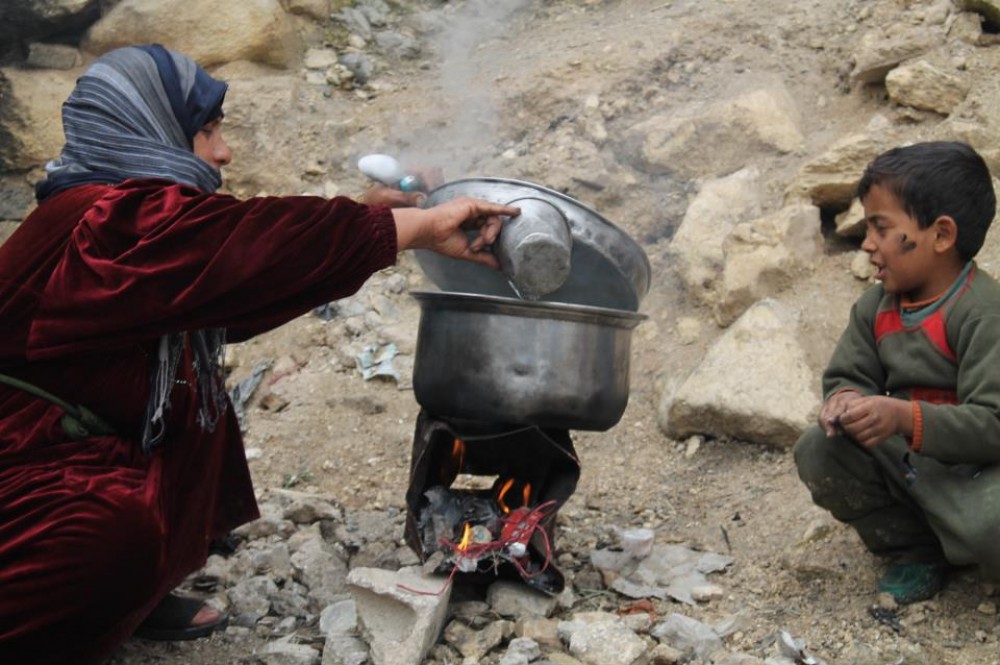 لاجئة فلسطينية بسوريا تطهو الطعام لأطفالها على النار 