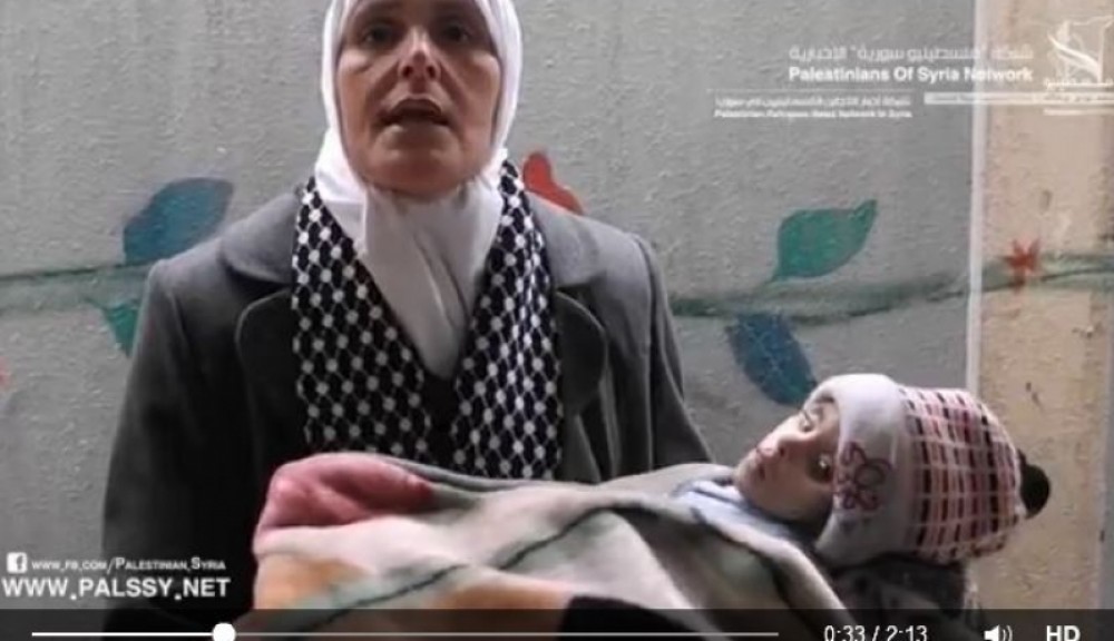 لاجئة فلسطينية تحمل طفلا توفي نتيجة الجوع 